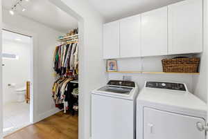 Laundry area with cabinet space, rail lighting, light wood-style floors, and washing machine and dryer