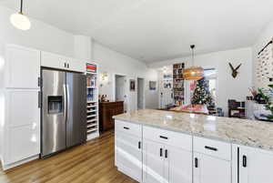 Kitchen with pendant lighting, white cabinetry, stainless steel refrigerator with ice dispenser, and light stone countertops