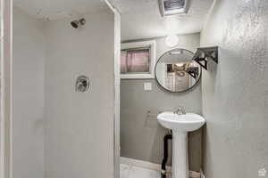 Full bath featuring a textured ceiling, marble look tile flooring, and tiled shower
