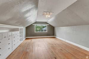 Additional living space with a textured ceiling, light wood-type flooring, vaulted ceiling, a textured wall, and built in shelves