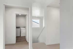 Hall featuring an upstairs landing, independent washer and dryer, light colored carpet, and a textured ceiling