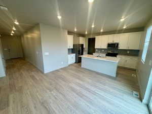 Kitchen featuring white cabinetry, open floor plan, light wood-style flooring, light countertops, and an island with sink