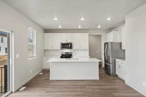 Kitchen with a kitchen island with sink, white cabinets, light wood-type flooring, appliances with stainless steel finishes, and recessed lighting