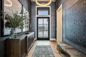 Doorway to outside with wallpapered walls, a chandelier, a high ceiling, and parquet flooring