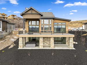 Rear view of property featuring stone siding, a balcony, a patio, and board and batten siding