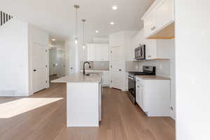 Kitchen featuring stainless steel appliances, white cabinets, an island with sink, and light wood-style floors