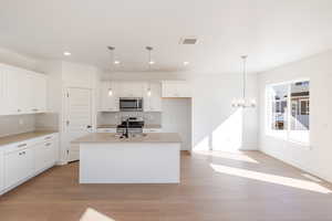 Kitchen featuring white cabinets, a chandelier, an island with sink, light wood-style flooring, and stainless steel appliances
