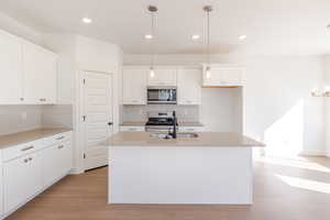Kitchen featuring hanging light fixtures, white cabinets, an island with sink, and stainless steel appliances