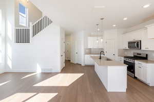 Kitchen with stainless steel appliances, white cabinets, a kitchen island with sink, dark wood-style flooring, and backsplash