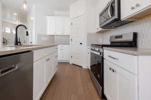 Kitchen featuring stainless steel appliances, white cabinets, dark wood-style flooring, decorative light fixtures, and tasteful backsplash