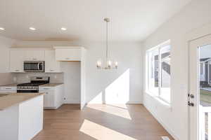 Kitchen featuring white cabinetry, stainless steel appliances, suspended lighting, light wood-style floors, and tasteful backsplash