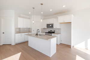 Kitchen with stainless steel appliances, light wood-type flooring, white cabinetry, and an island with sink
