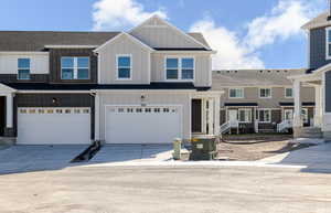 View of front of house with board and batten siding, driveway, an attached garage, and a shingled roof