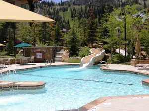 Community pool featuring a patio, a water slide, stairs, and a view of trees