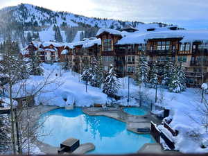 Snow covered pool featuring a hot tub, a community pool, a patio, and a mountain view