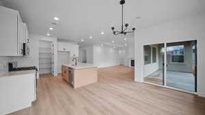 Two tone kitchen featuring dual tone cabinets, a center island with sink, stainless steel appliances, a chandelier, and light wood finished floors