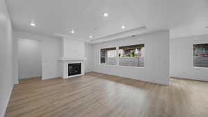 Unfurnished living room with a large fireplace, a tray ceiling, light wood finished floors, and recessed lighting