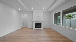 Unfurnished living room with light wood-style flooring, a fireplace, recessed lighting, and a raised ceiling