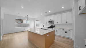 Dual tone kitchen featuring stainless steel appliances, an island with sink, light wood-style flooring, light stone countertops, and two tone cabinetry