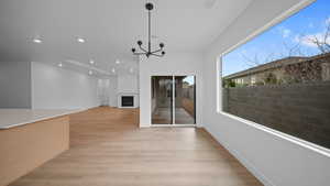 Unfurnished dining area featuring a chandelier, light wood-style floors, and a large fireplace