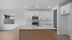 Kitchen with an island with sink, light stone countertops, stainless steel appliances, light wood-type flooring, and dual tone cabinets