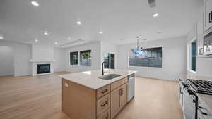 Kitchen with a large fireplace, open floor plan, light stone countertops, a kitchen island with sink, and light wood-type flooring