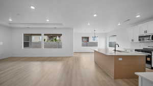 Kitchen with stainless steel appliances, dual tone cabinets, light wood-style floors, decorative backsplash, and a center island with sink