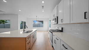 Two tone kitchen with stainless steel appliances, dual tone cabinetry, light wood-type flooring, light stone counters, and backsplash