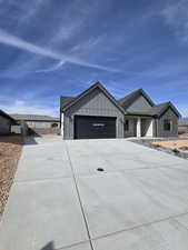 View of front facade with board and batten siding, concrete driveway, an attached garage, and stone siding