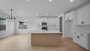 Kitchen featuring stainless steel appliances, a center island with sink, light wood-style floors, suspended lighting, and light stone countertops