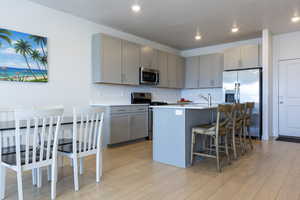 Kitchen featuring gray cabinets, appliances with stainless steel finishes, a center island with sink, a breakfast bar, and recessed lighting
