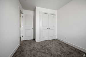 Unfurnished bedroom featuring dark carpet and a closet
