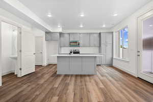 Kitchen with gray cabinetry, stainless steel microwave, a center island with sink, light wood-style flooring, and electric stove