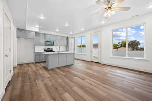 Kitchen featuring gray cabinets, stainless steel microwave, light wood-style flooring, electric range, and a kitchen island with sink