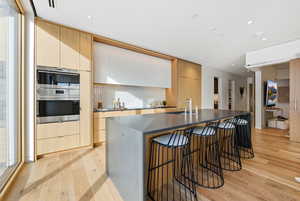 Kitchen featuring light brown cabinets, modern cabinets, an island with sink, a breakfast bar area, and light wood-style floors