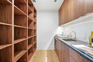 Bar with brown cabinets, light wood-style flooring, decorative backsplash, dark countertops, and modern cabinets