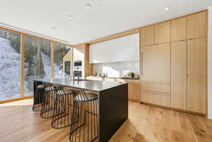 Kitchen featuring light brown cabinets, a breakfast bar, modern cabinets, light wood-type flooring, and a center island with sink