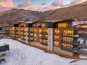 Snow covered property featuring a balcony, stone siding, and a mountain view