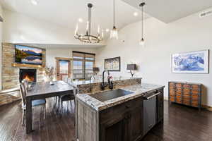 Kitchen with dark brown cabinets, pendant lighting, an island with sink, dark wood finished floors, and vaulted ceiling