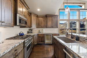 Kitchen featuring appliances with stainless steel finishes, light stone countertops, wine cooler, decorative light fixtures, and a textured ceiling