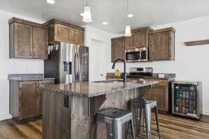 Kitchen with hanging light fixtures, beverage cooler, stainless steel appliances, a center island with sink, and a breakfast bar