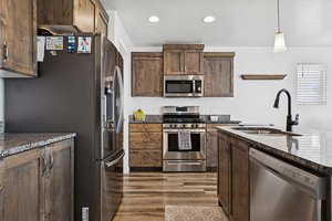 Kitchen featuring stainless steel appliances, recessed lighting, pendant lighting, dark brown cabinetry, and dark stone counters