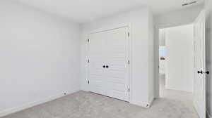 Unfurnished bedroom featuring light colored carpet and a closet