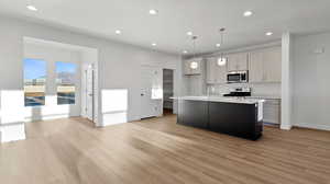 Kitchen featuring a center island with sink, pendant lighting, recessed lighting, appliances with stainless steel finishes, and light wood-type flooring