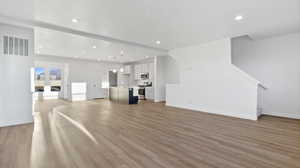Unfurnished living room featuring light wood finished floors, recessed lighting, and stairs