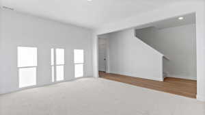 Unfurnished living room featuring stairs and light colored carpet