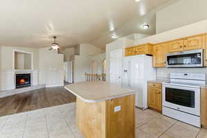 Kitchen with white appliances, light countertops, a tile fireplace, vaulted ceiling, and a kitchen island