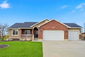 Ranch-style home featuring covered porch, a front yard, an attached garage, and concrete driveway