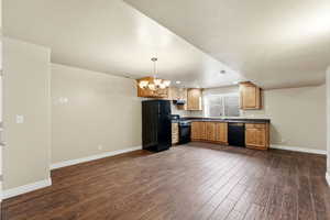 Kitchen with dark countertops, black appliances, a chandelier, and dark wood-type flooring