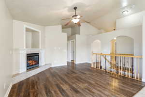 Unfurnished living room with dark wood-style floors, a tiled fireplace, lofted ceiling, and a ceiling fan